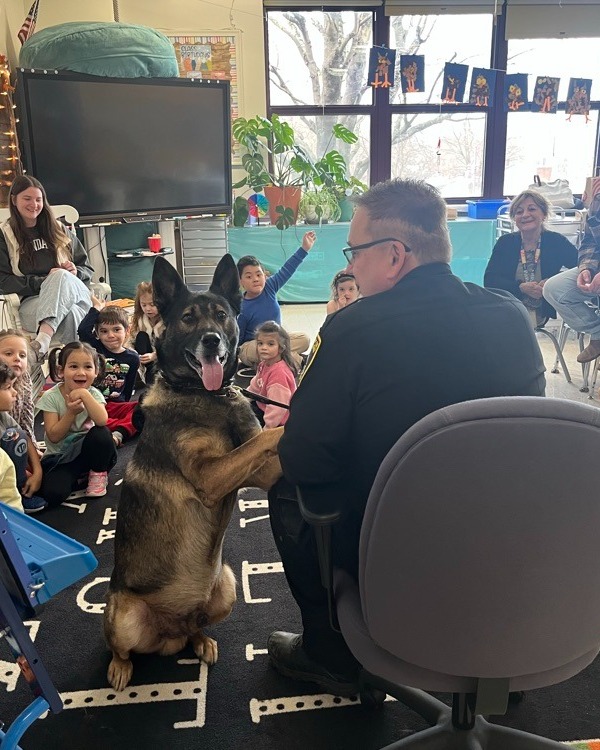 A dog looks at the camera as a group of children behind it smile