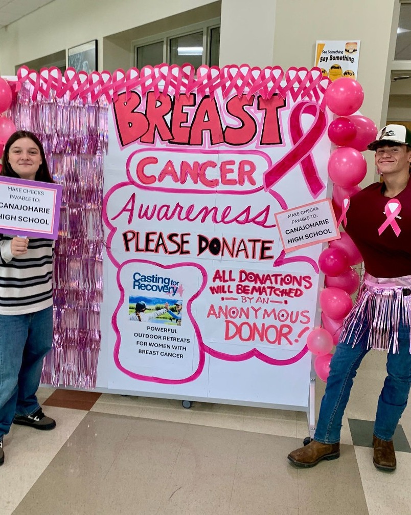 Two students stand next to a poster about Breast Cancer Awareness