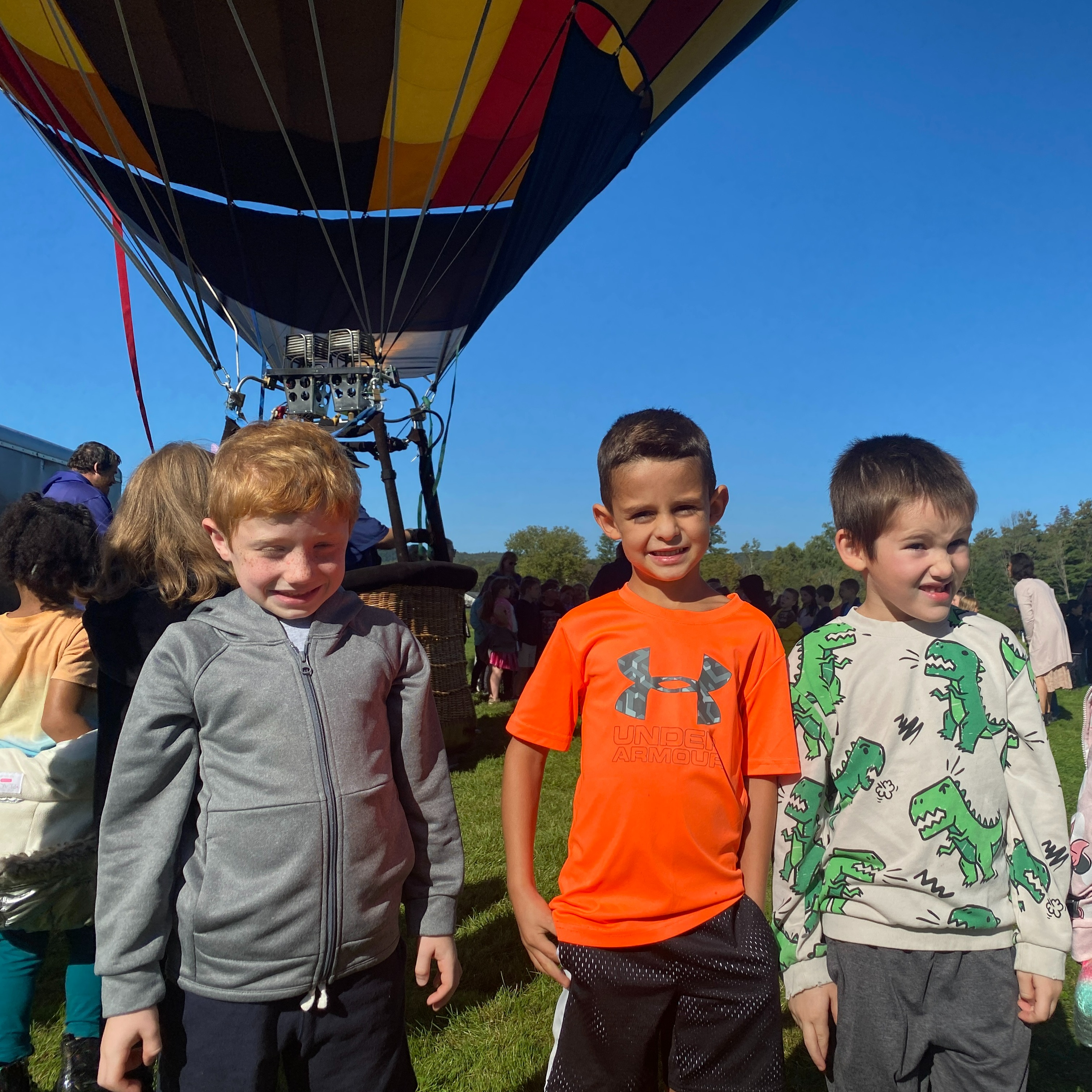 Three children stand in front of a hot air balloon