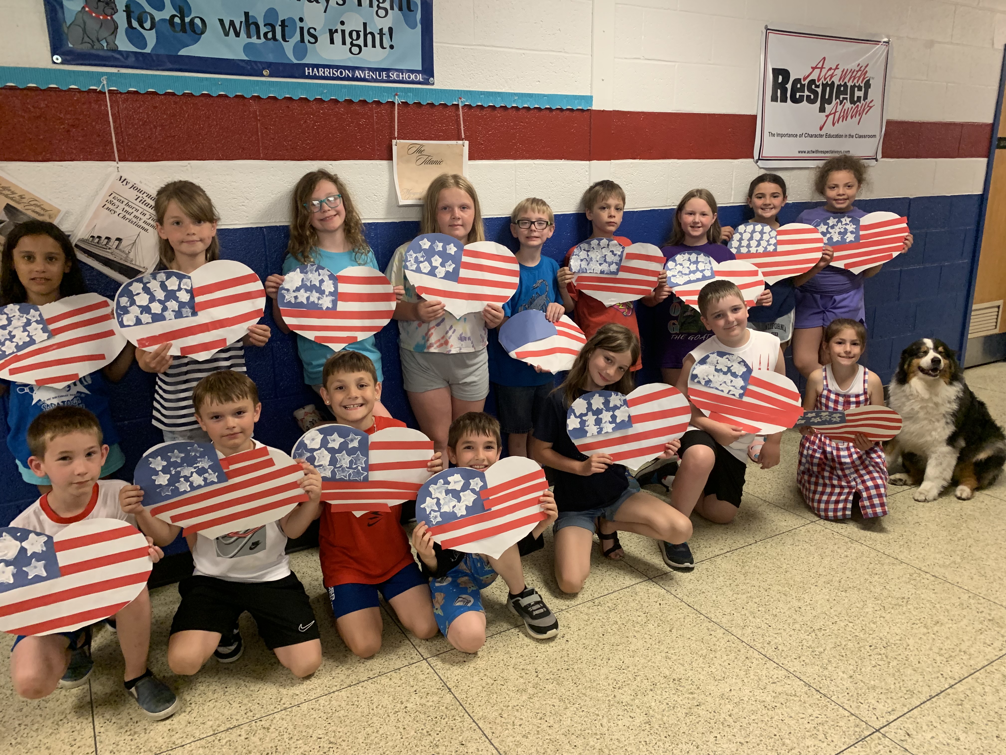 About a dozen students hold red, white and blue heart-shaped art projects