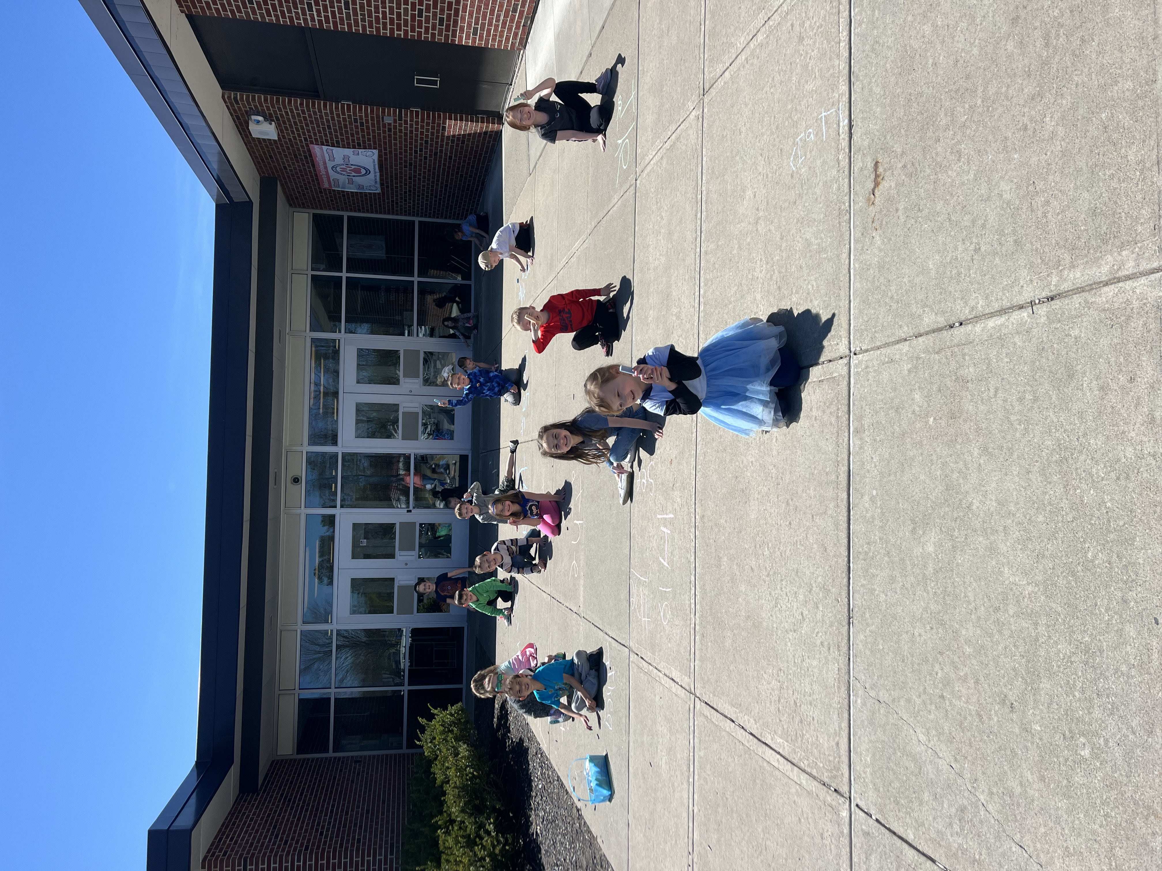 Children create chalk art in front of the building