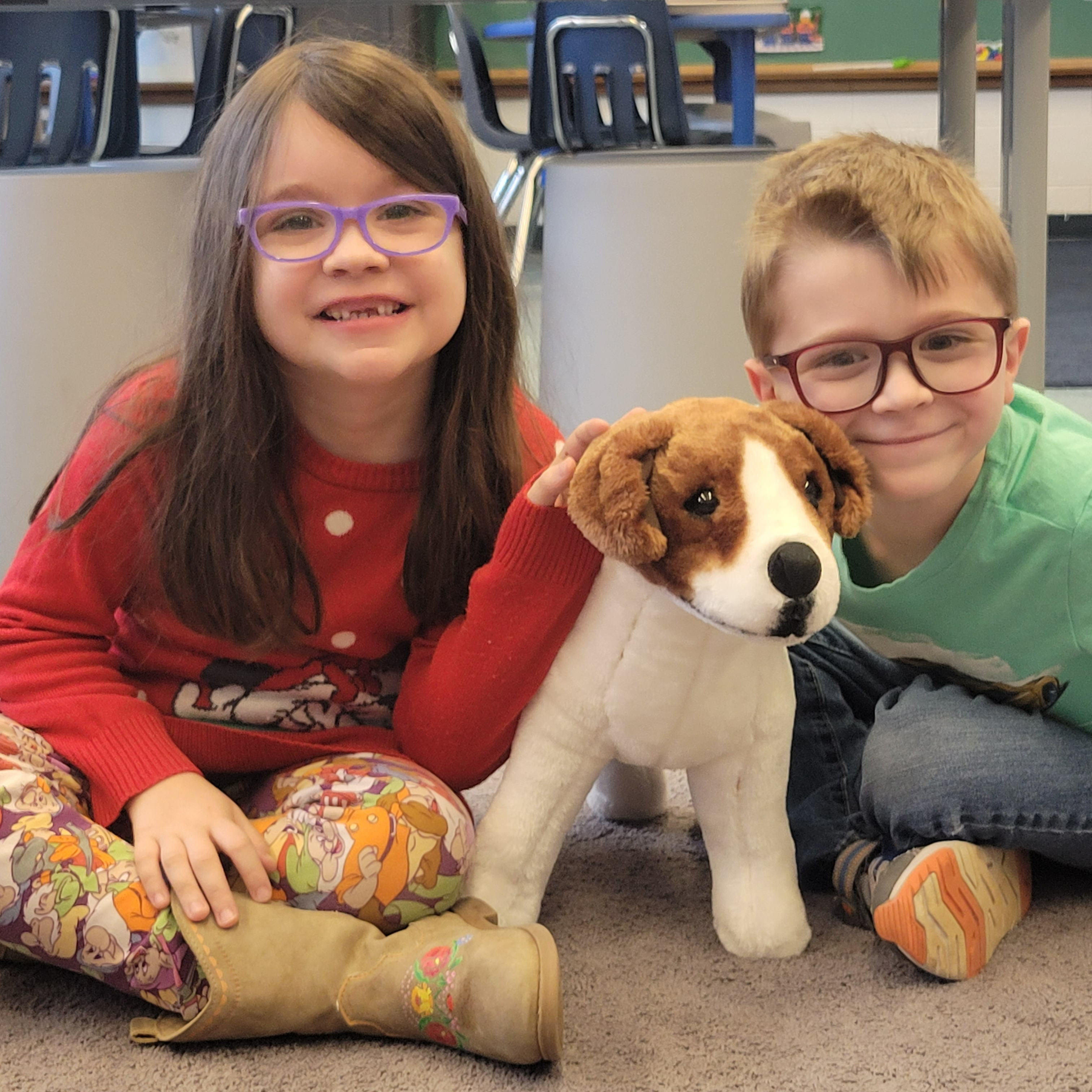 Two students sit smiling with a stuffed dog between them. 