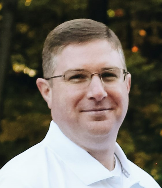 Standing wearing a white shirt and glasses