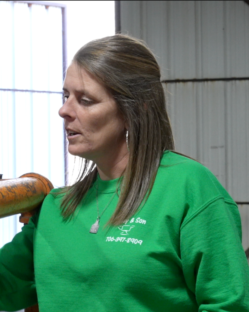 A woman in a green shirt is near a horse with a blue rope, standing inside a barn.