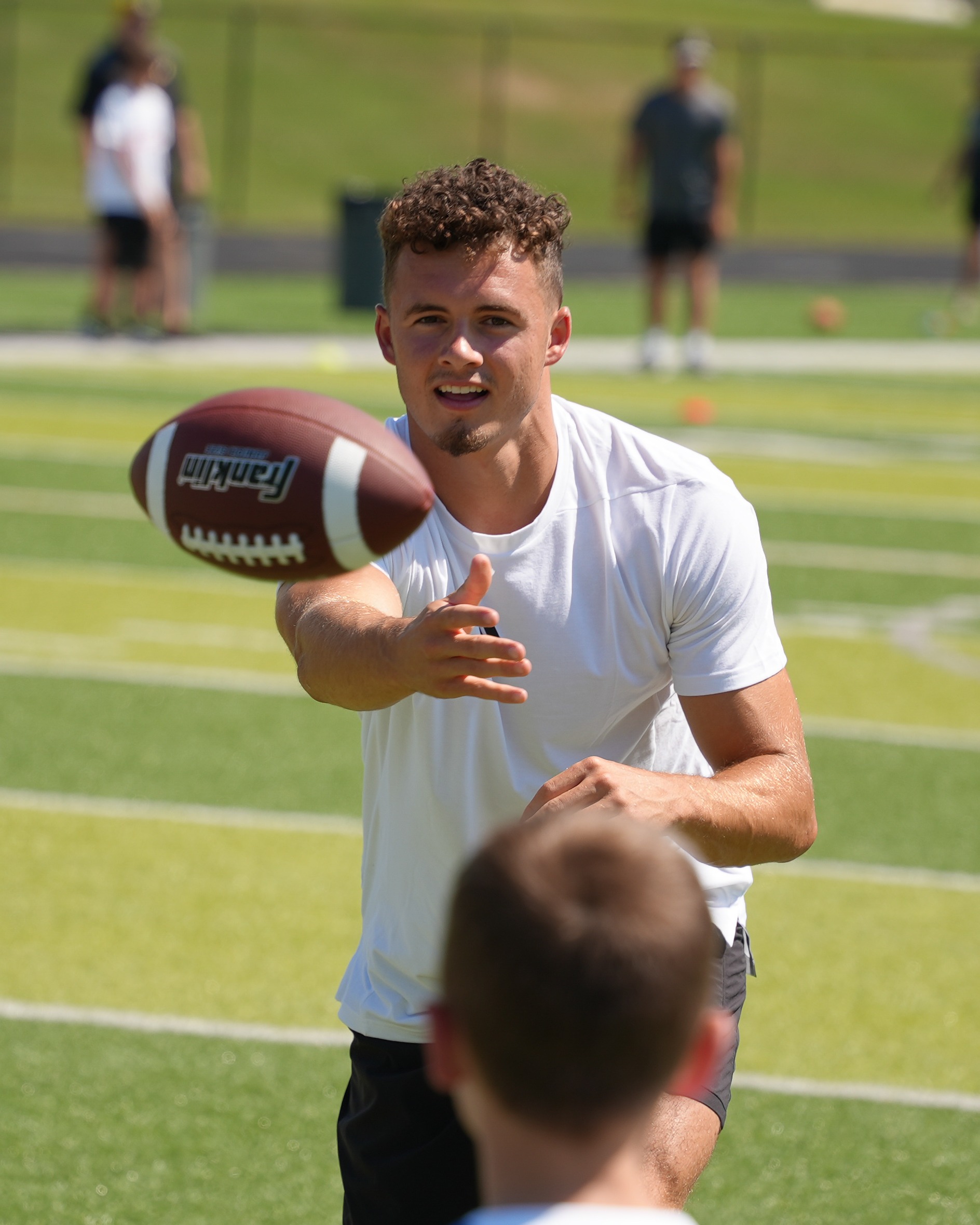 A person throws a football to another person during a football practice on a field.