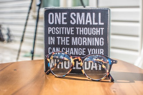 A photo of a pair of glasses in a table with the phrase "One small positive thought in the morning can change your whole day" in the back.