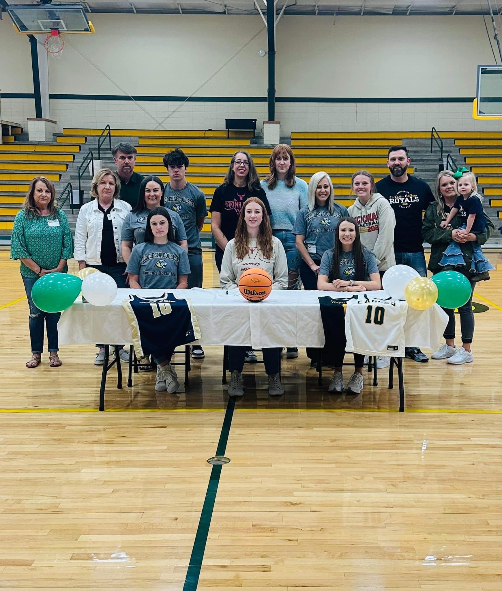 students sitting at table with their family members behind them