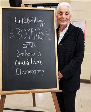 Barbara stands next to a chalk board that says celebrating 30 years 
