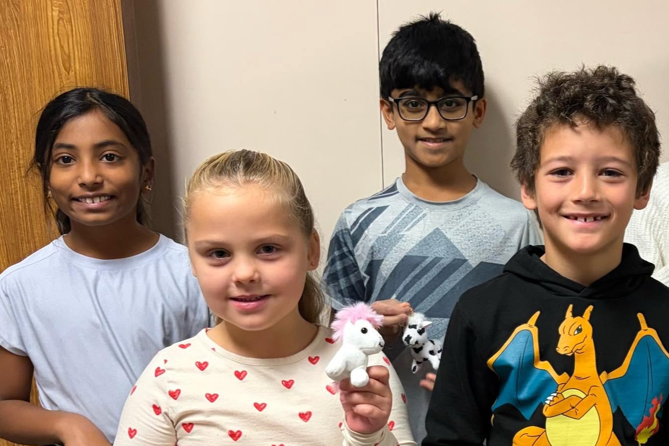 four students- two girls two boys smiling with tiny plush horses