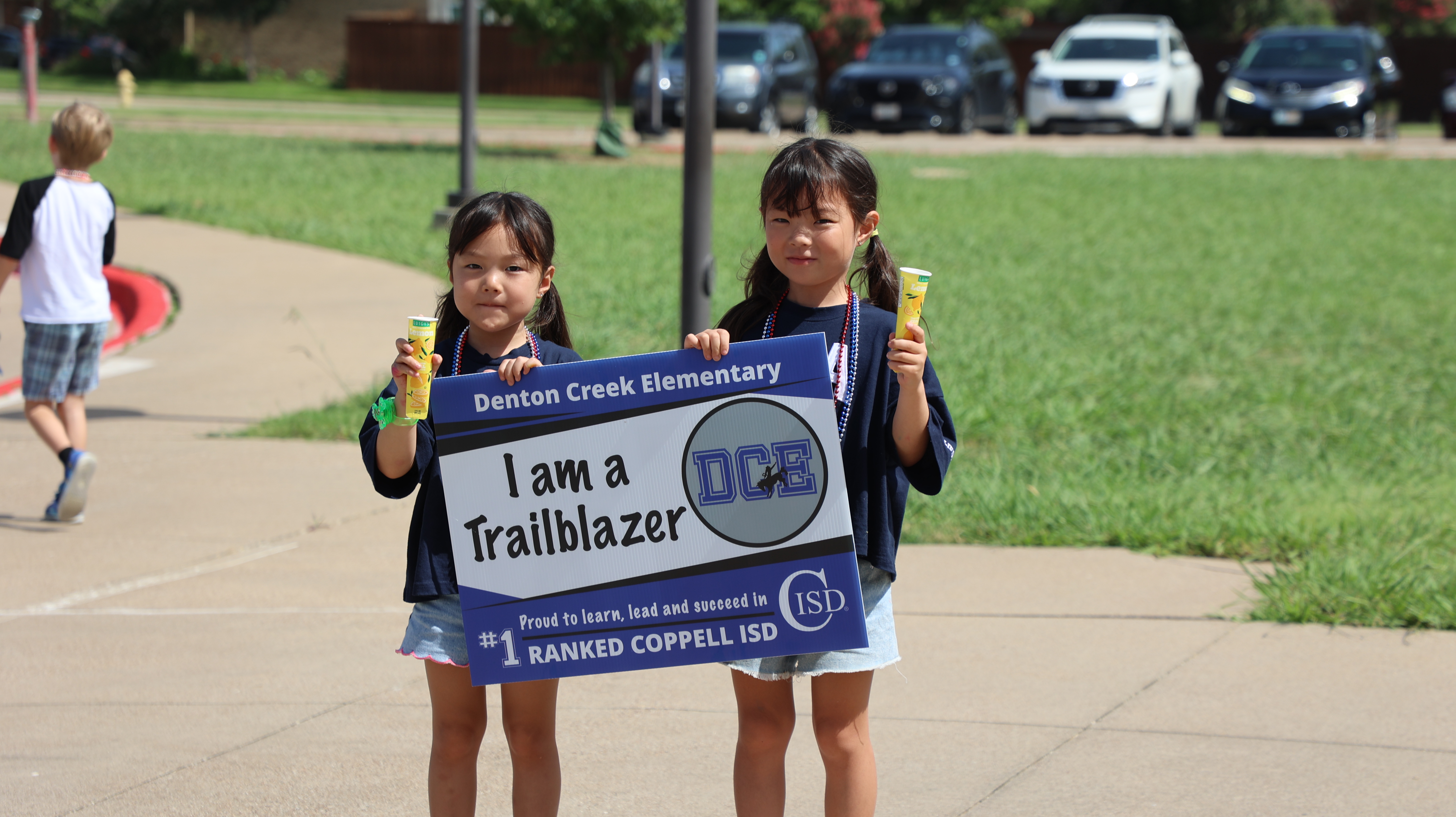 Two student holding a popsicle and a sign that reads Denton Creek Elementary, I am a Trailblazer and Proud to learn, lead and succeed in #1 Ranked Coppell ISD.