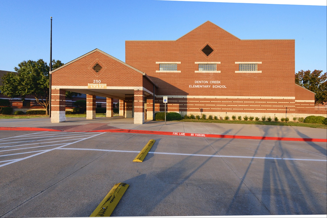 Brick building labeled "Denton Creek Elementary School" with a front entrance and parking lot in the foreground.