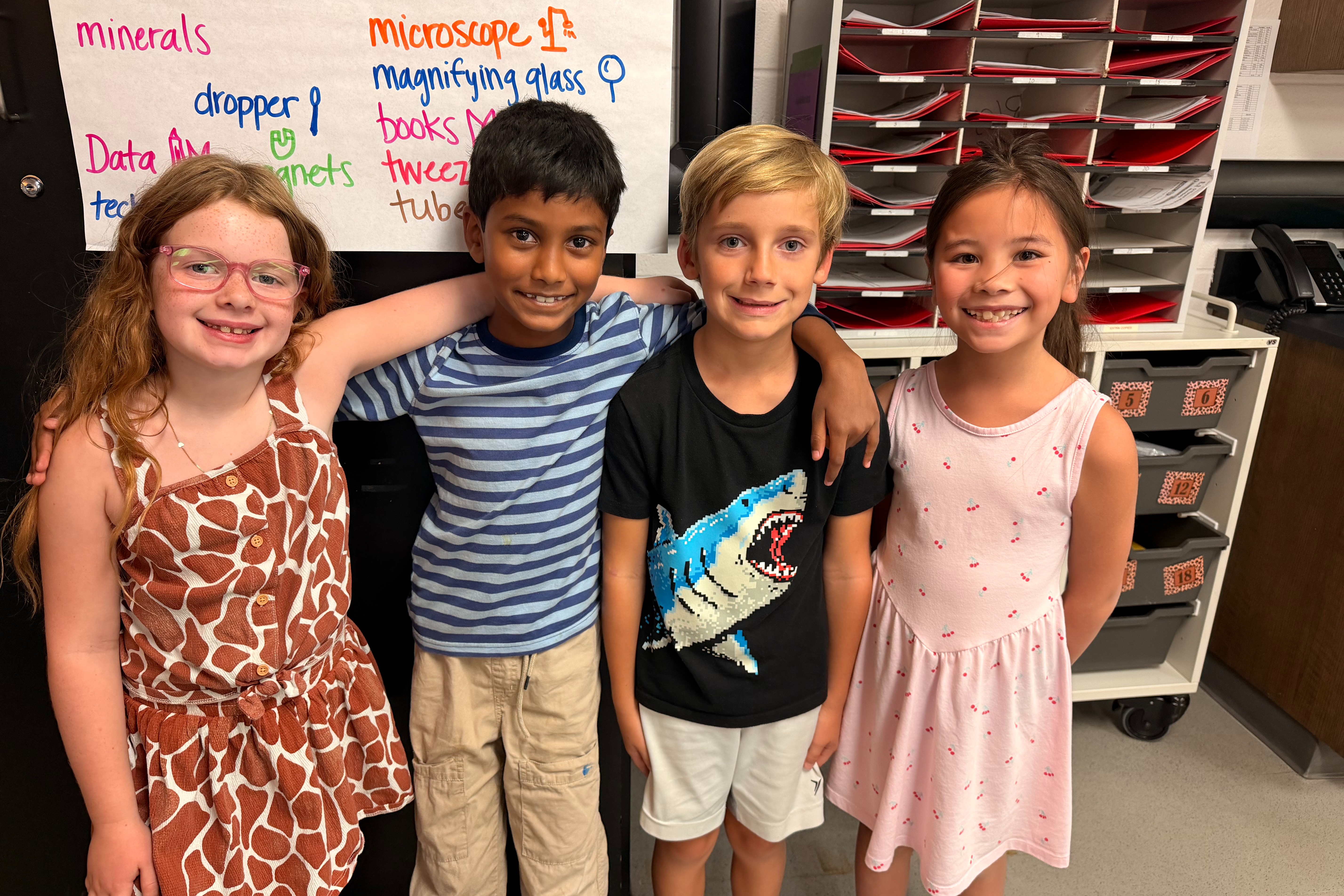 This image shows three second grade learners standing in their classroom in front of a closet.