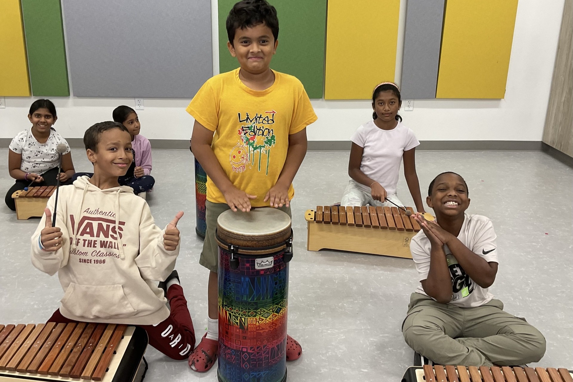 Group of students, all smiling. They are playing xylophones and drums in music class.