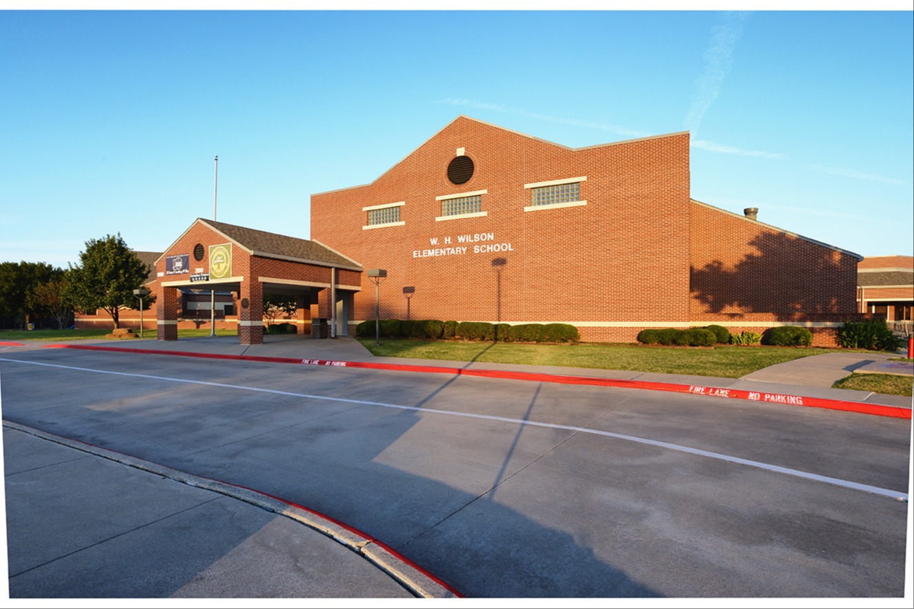 Brick building labeled "W. H. Wilson Elementary School" with a covered entrance and fire lane curb marked "Fire Lane No Parking" in the foreground.
