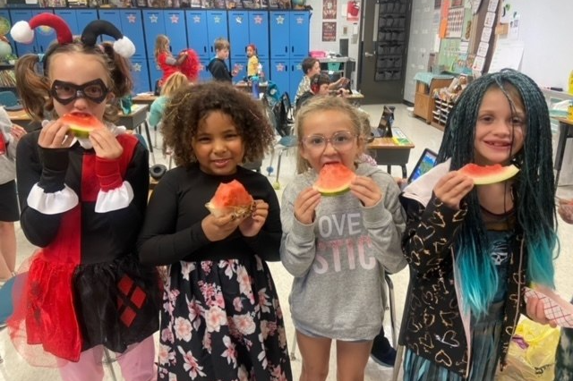 A image of 4 children eating watermelon in a classroom.