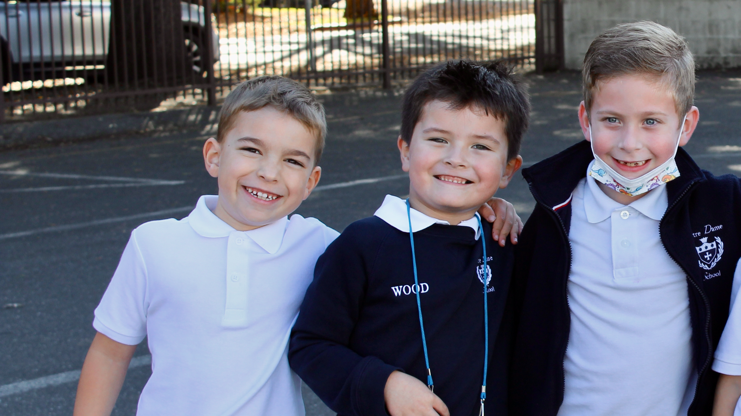 three boys smiling in school uniforms, in the sun
