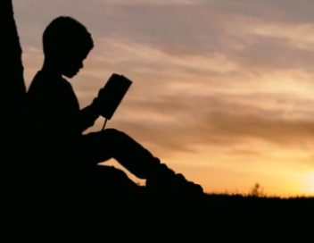 silhouette of child reading a book with sunset in background