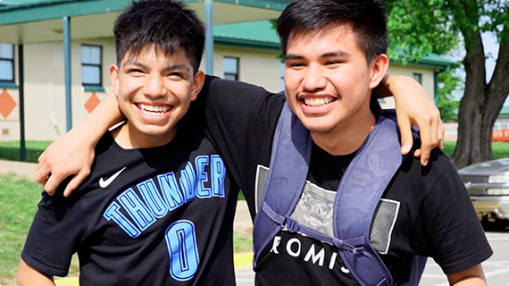 2 students smiling for the camera with their arms around each other's necks