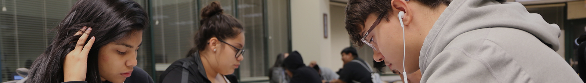 Three students at a table together, focused on their individual assignments