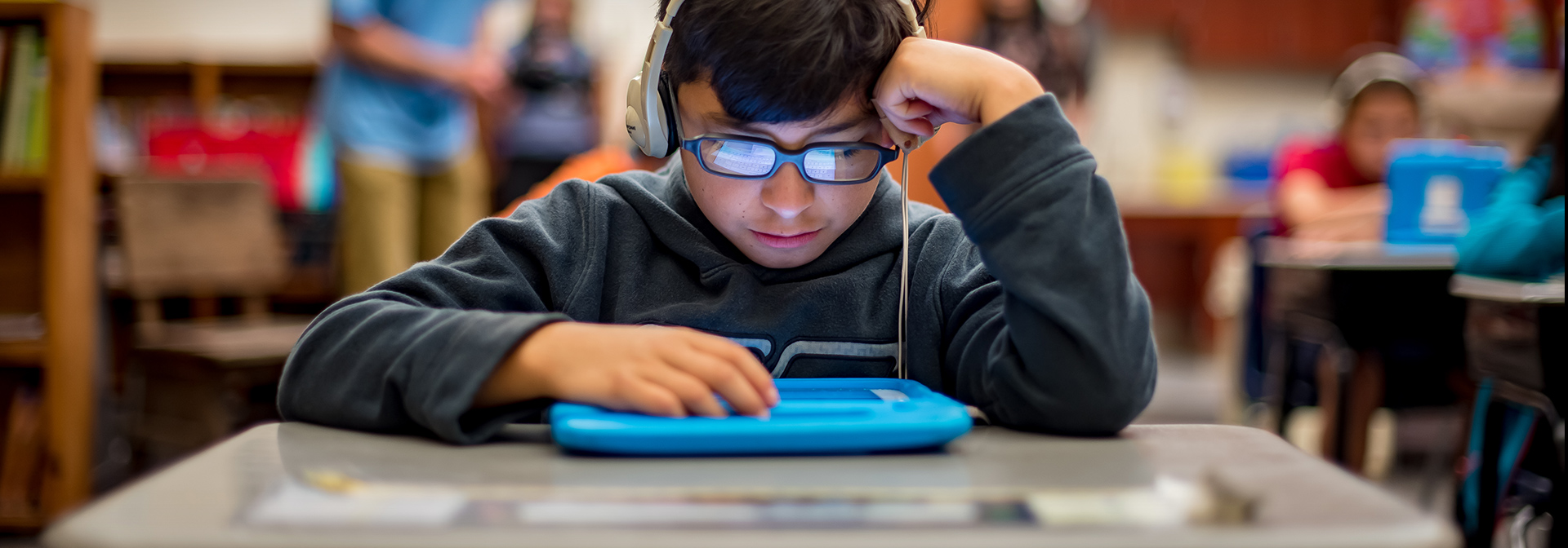 A student looking down at a tablet while wearing headphones