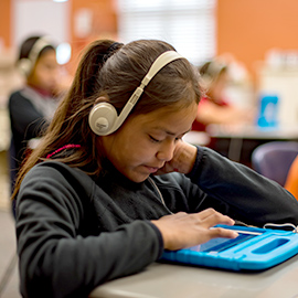 A young student looking at a tablet with headphones on