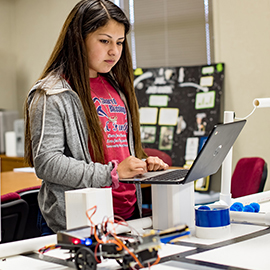 A student working on a project with a laptop and supplies