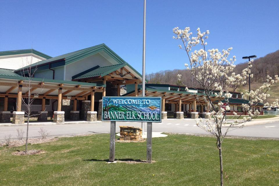 The school sign outside of the front entrance to the school. It is a sunny day and there is a white flowering tree in the foreground.