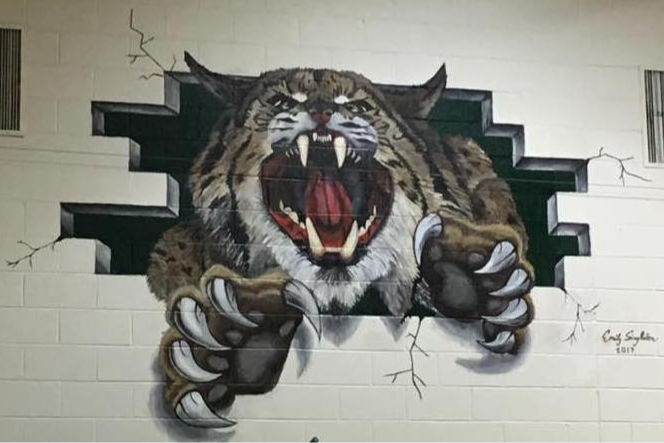 A painted mural of a wildcat breaking through a brick wall.