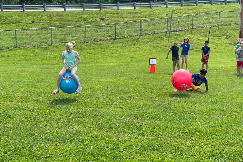 students outside on a clear day  riding large bouncy balls  in a field day race