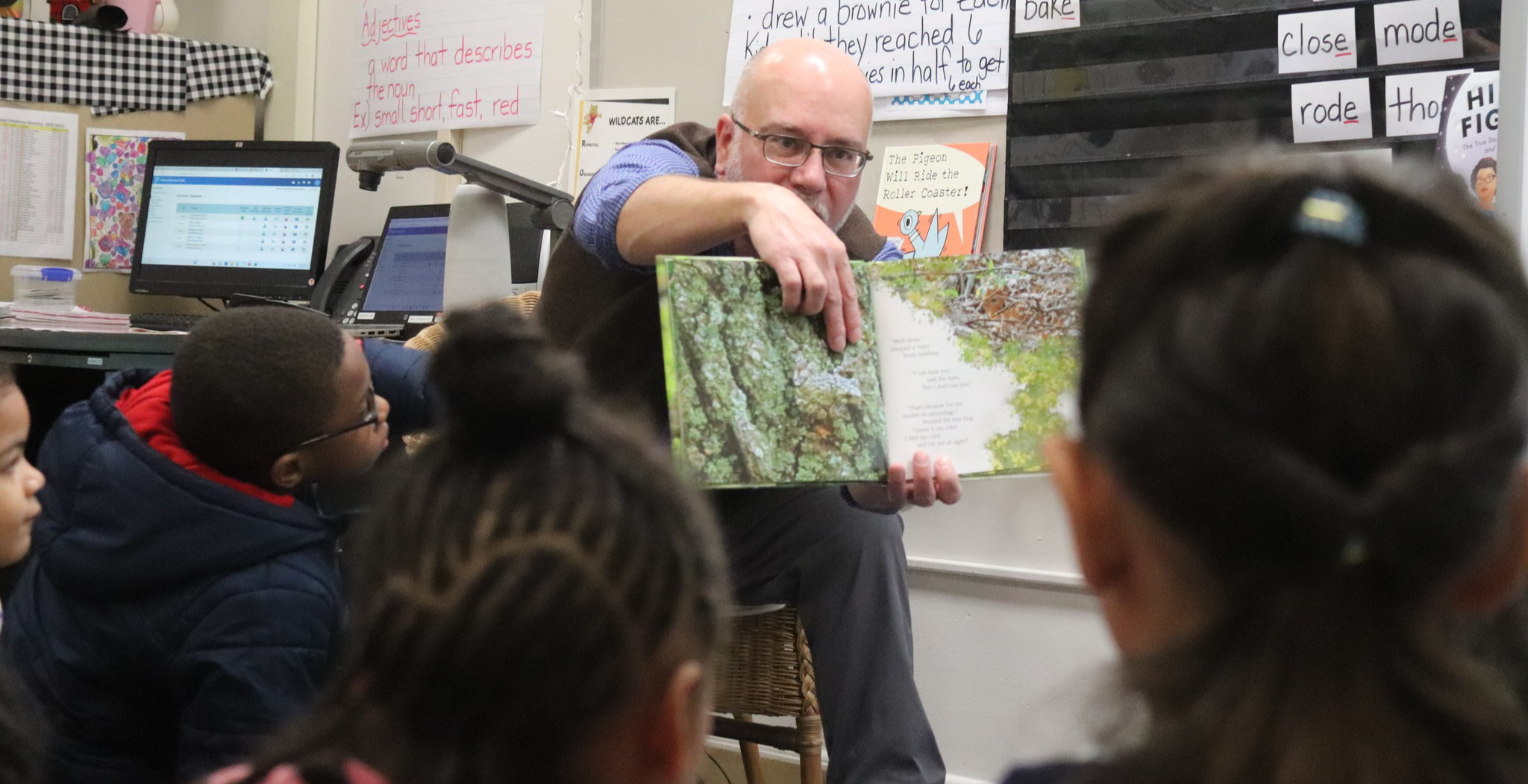 A man points to a page in a book as students look on