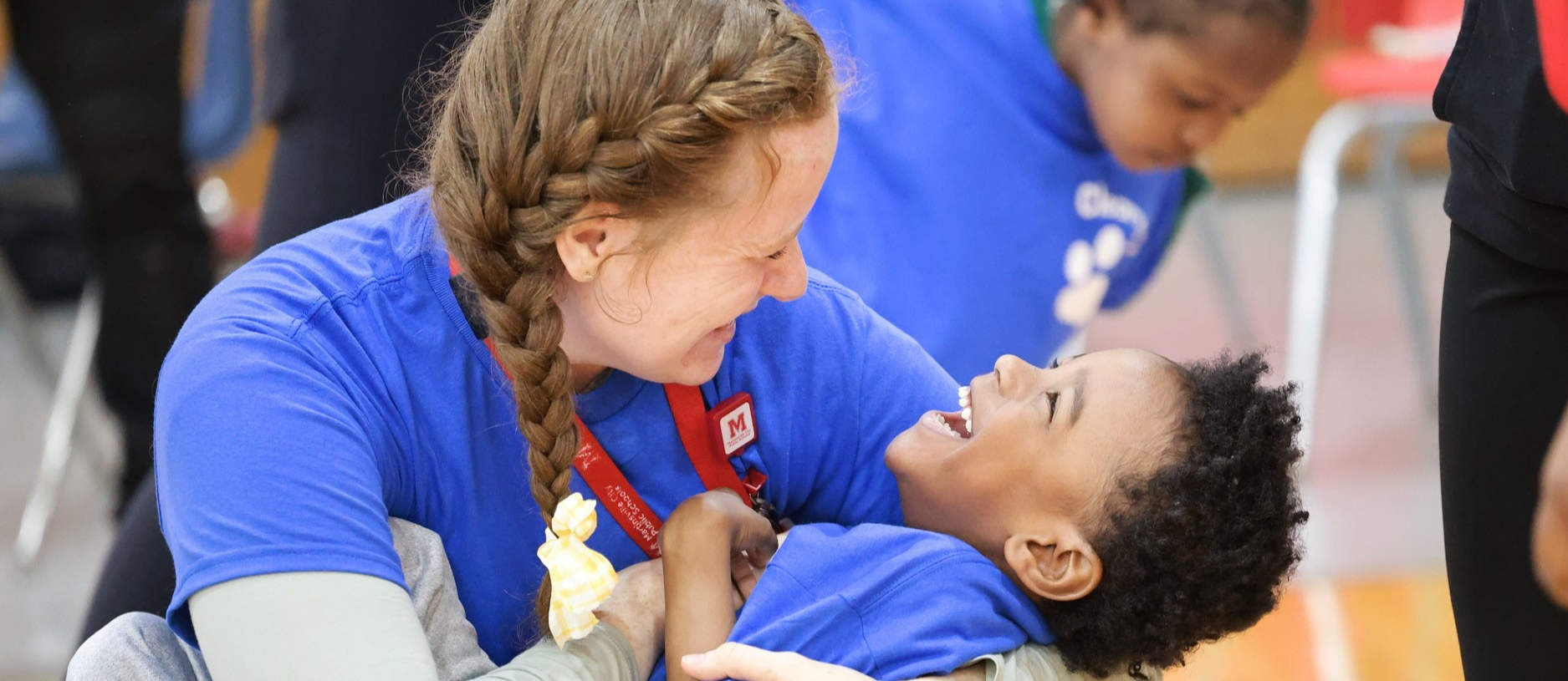 A teacher smiles broadly while holding a preschool student, who smiles back
