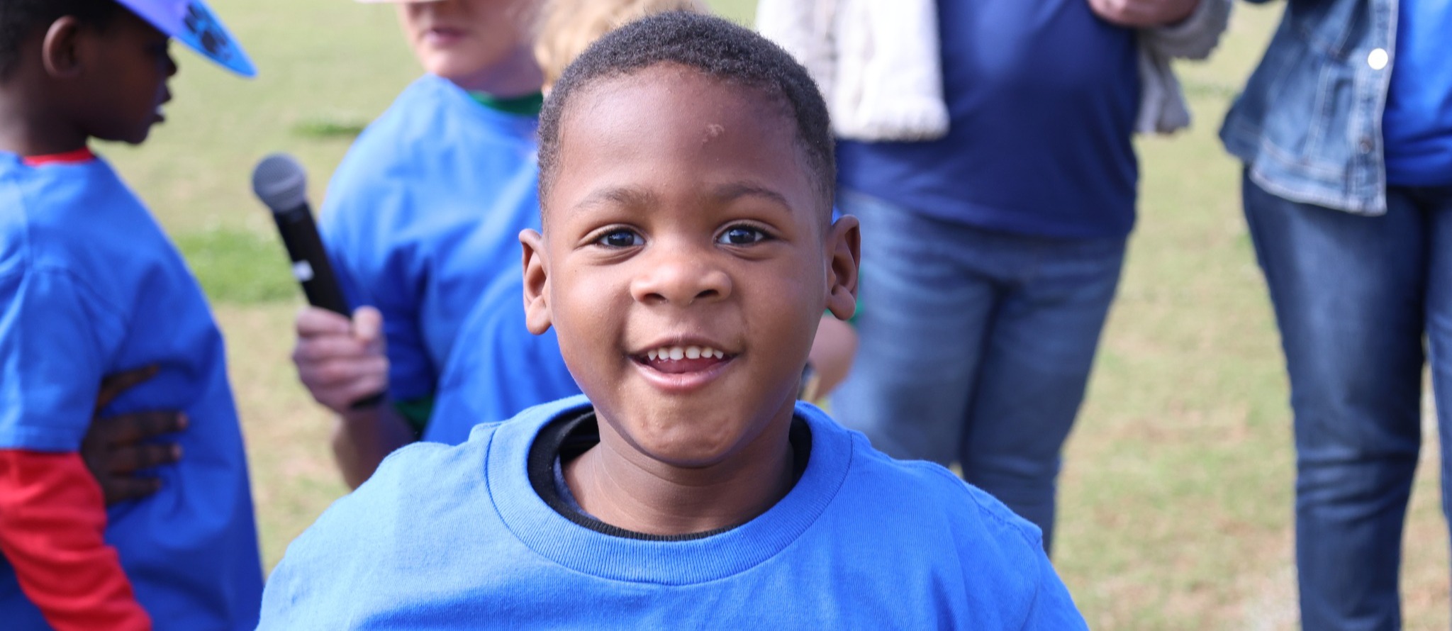 A preschool student smiles broadly outside on a football field
