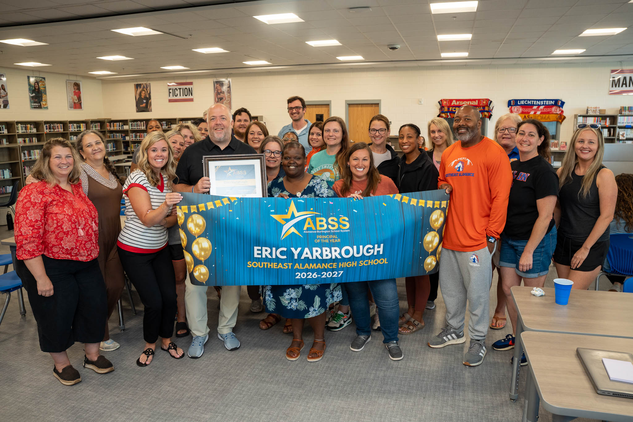Principal Eric Yarbrough stands with staff behind a Principal of the Year banner
