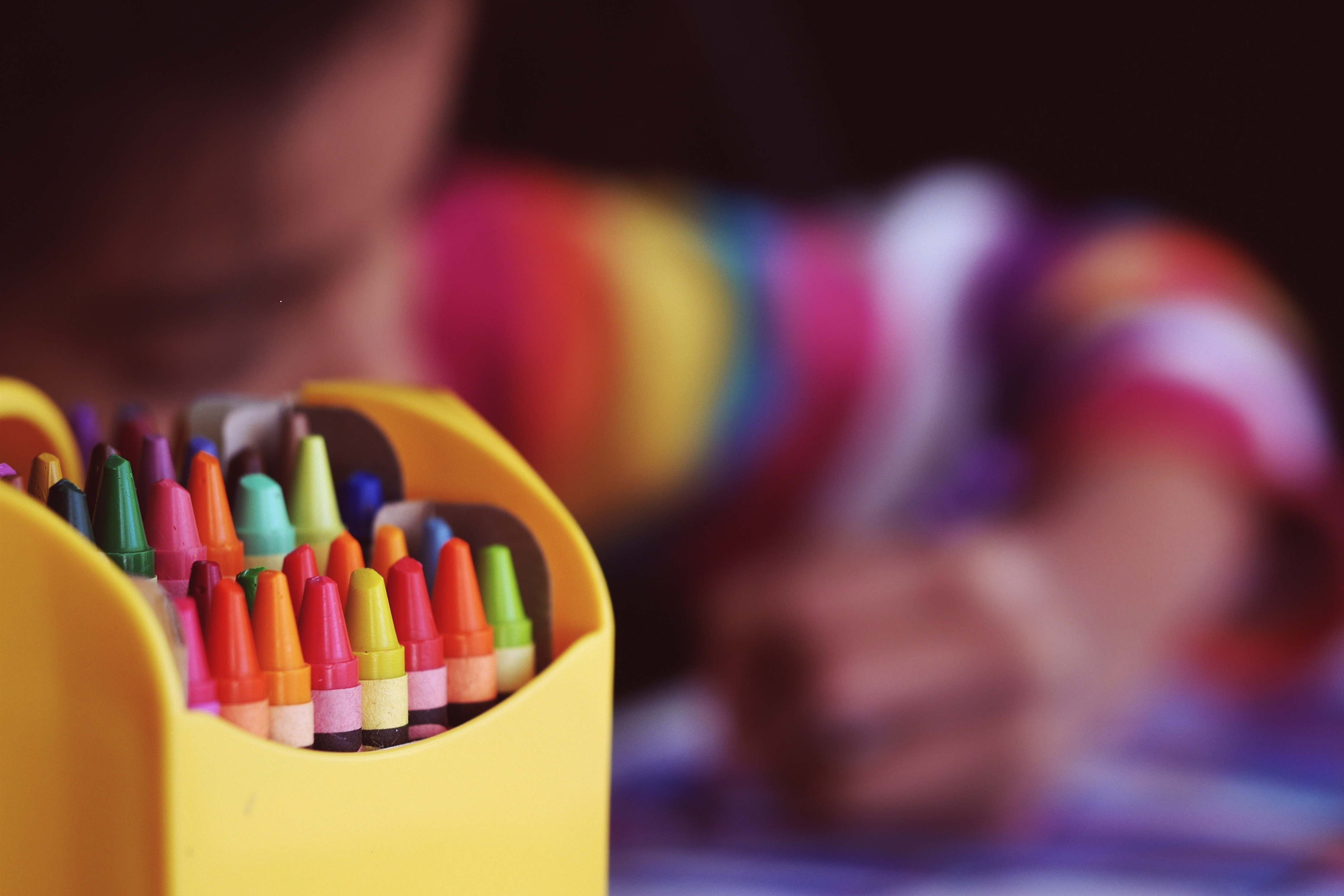 yellow box of colorful crayons with a blurred background of a child in a colorful sweater coloring on a piece of paper