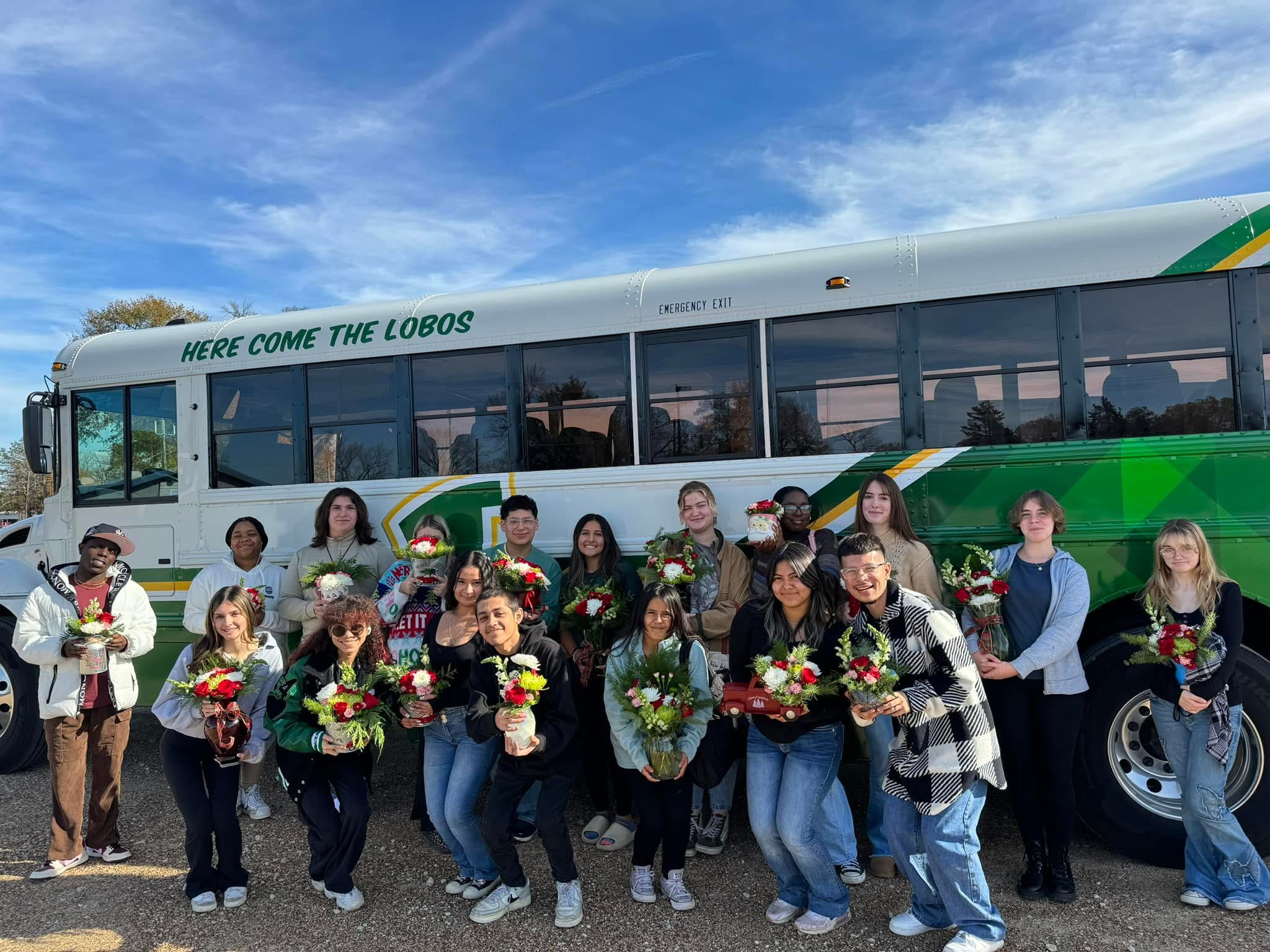 Students holding floral arrangements in front of a green-and-white Lobo bus.