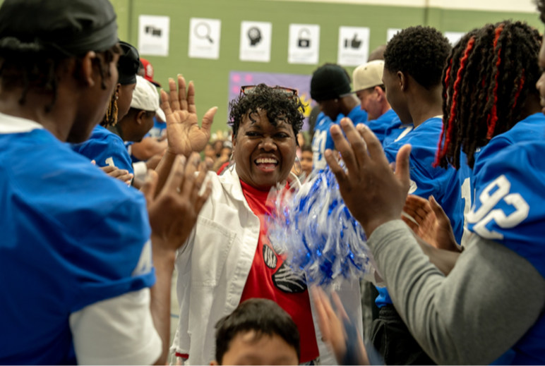 A smiling woman walks between people in blue jerseys offering high-fives.