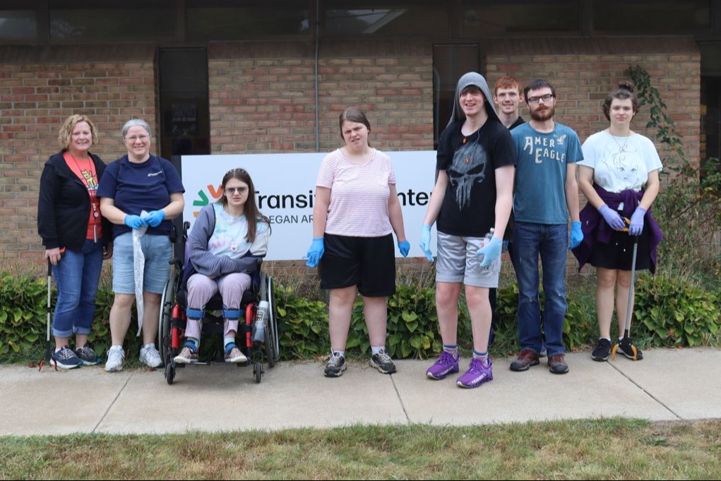 Two teachers pose in front of school sign with 6 students