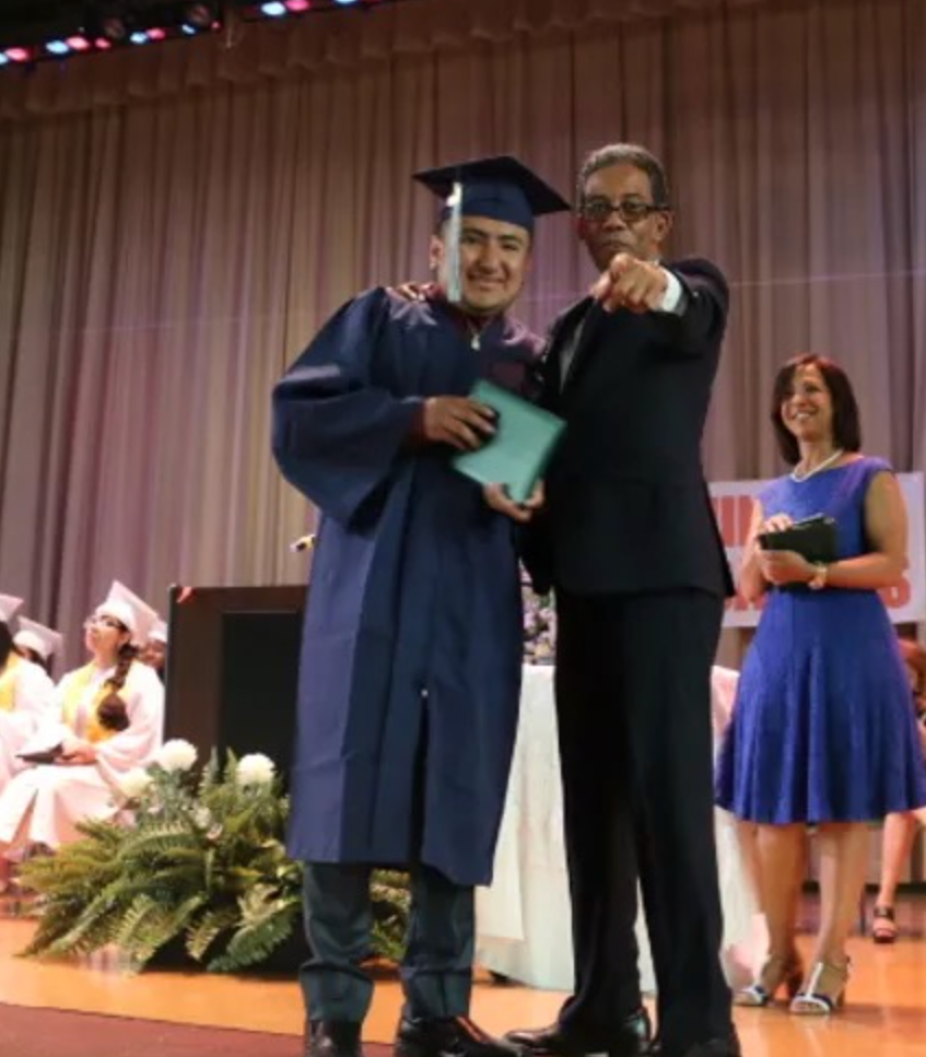 Student in cap & gown posing for graduation with faculty member