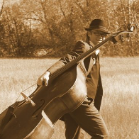 A brown monochrome photo of Don pulling a large stringed instrument through a field 