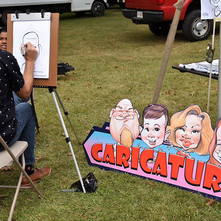 white male drawing caricature cartoons with large sign and easel