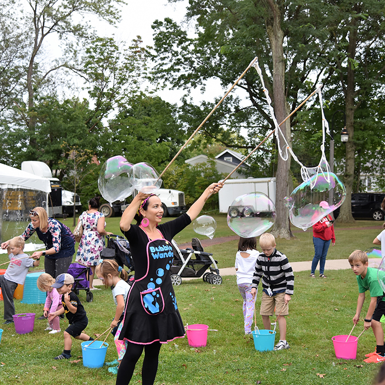 white female making large bubbles with wands with kids