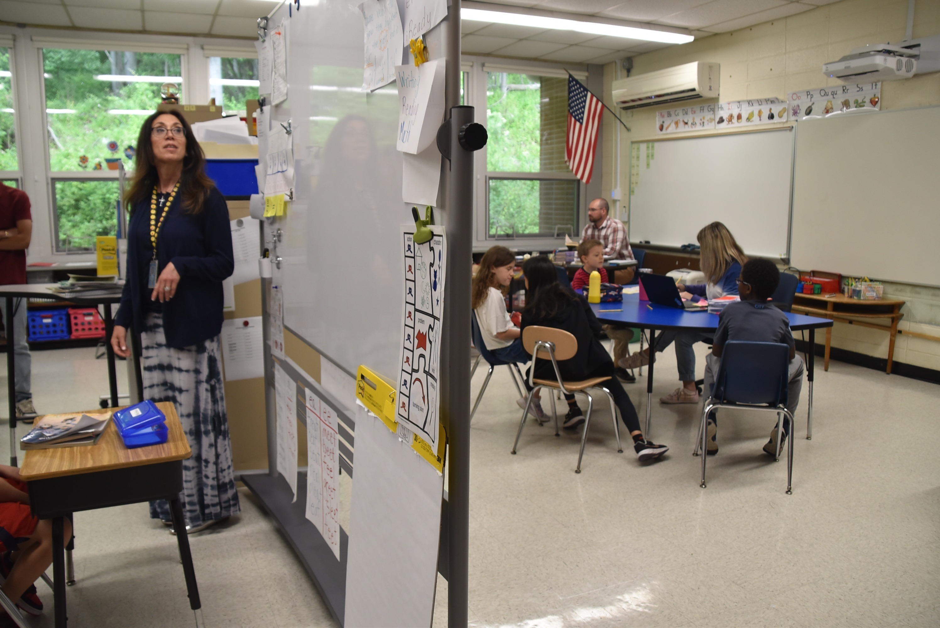 A write-and-wipe board divides a single classroom so teachers can simultaneously present unrelated lessons on both sides of it. Classrooms throughout the district are divided into 2, 3 and sometimes 4, in order to make room for several classes to meet at the same time in the same space. The dividers between classes are temporary bulletin boards that do little to filter out distractions.