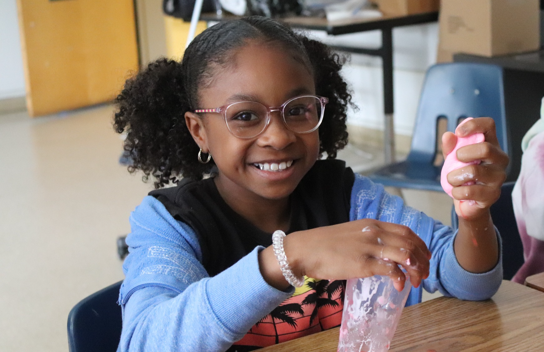 AHES student sits at desk in classroom with cup of homemade slime