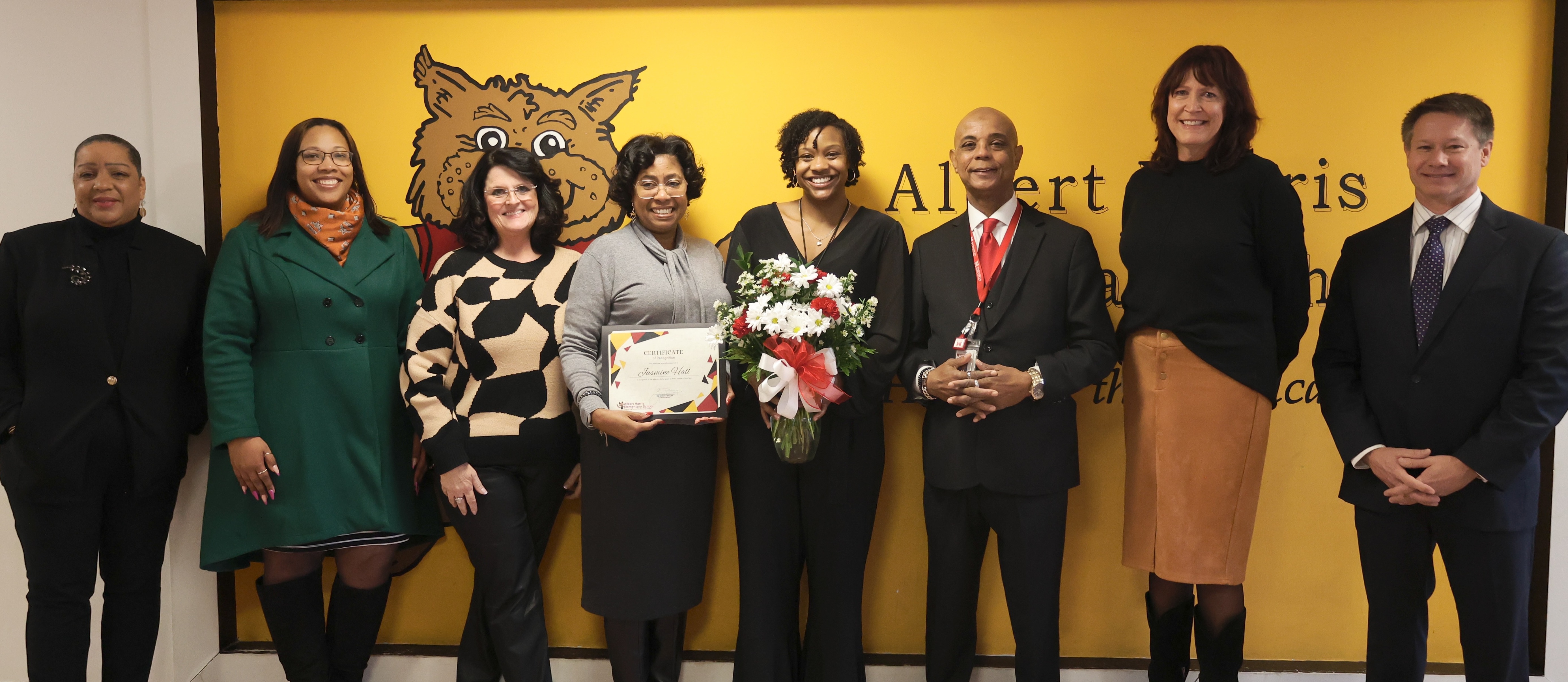 Jasmine Hall, teacher, smiles broadly as she holds a bouquet of flowers and stands among MCPS and AHES administrators