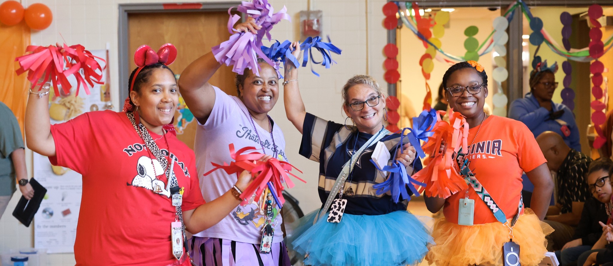 Teachers dressed in bright colors smile and wave paper pom poms