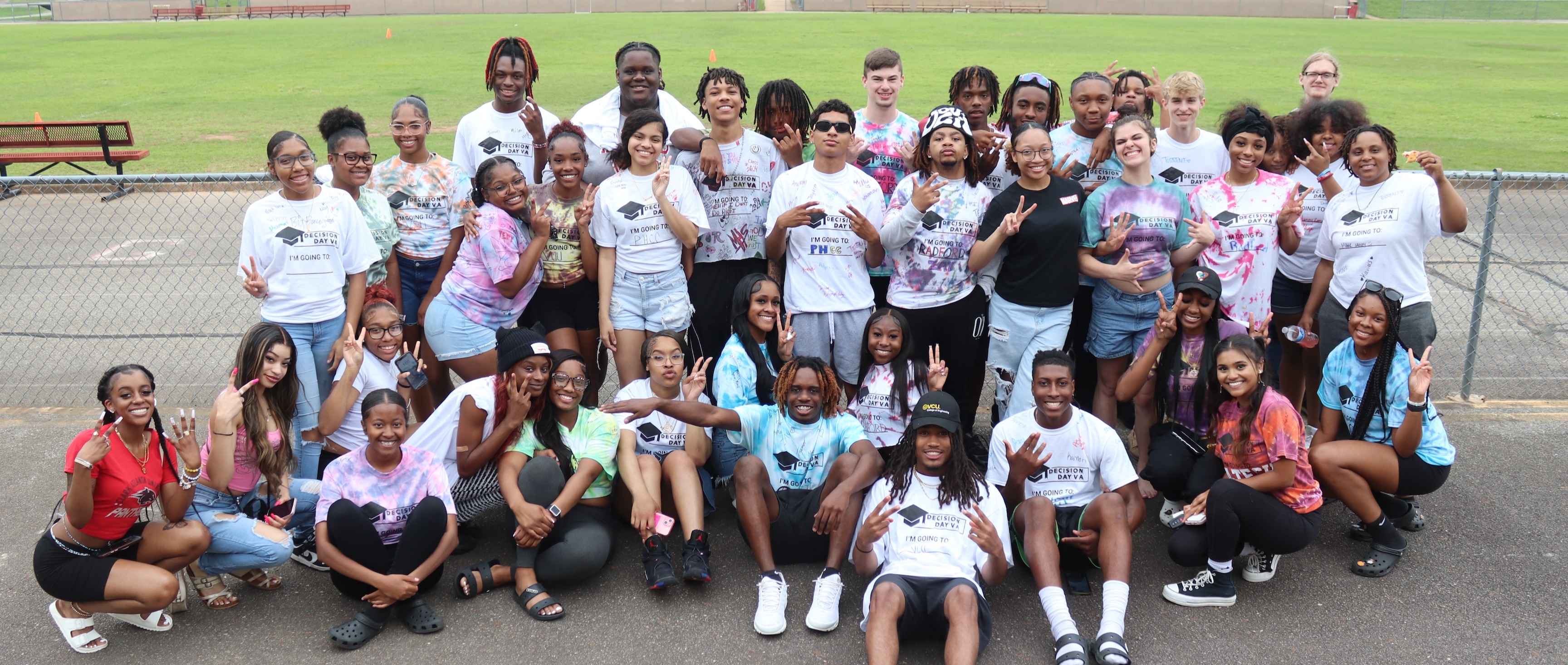 A group of high school seniors in tye-dye t-shirts pose for a group photo on the football field