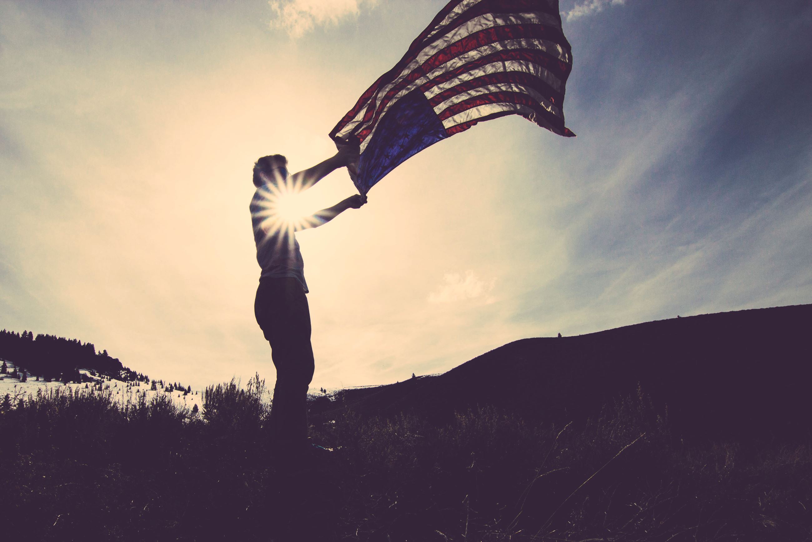 A photo of a silhouetted person waving an American flag with the sun behind them