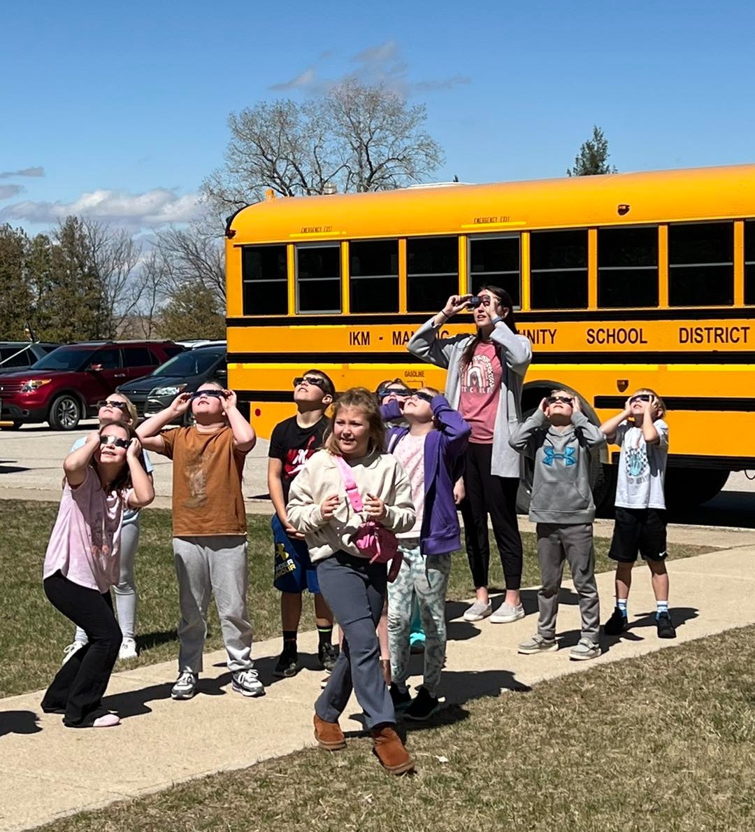 Students viewing the eclipse with special glasses. in front of a school bus