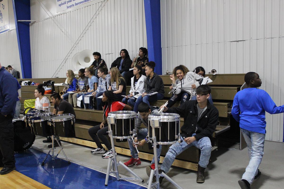 Band students at an indoor game waiting to play while watching.