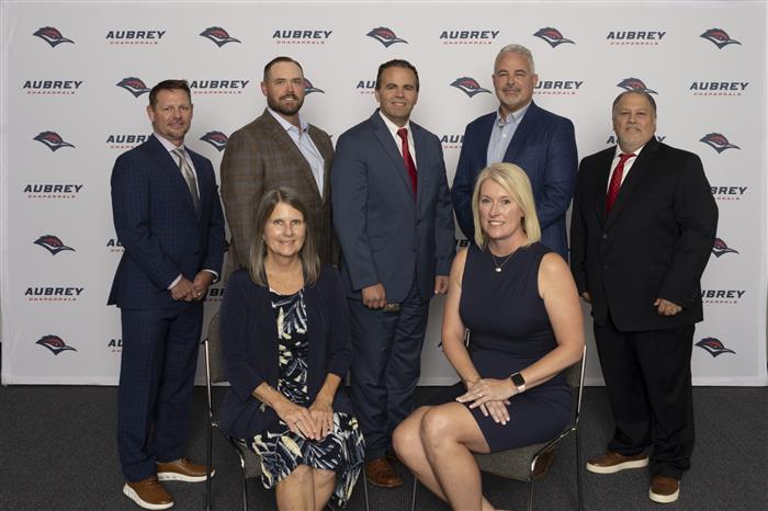 School board members posing in front of Aubrey ISD themed background